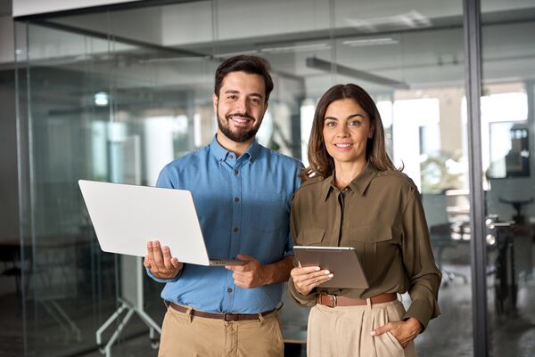 Two,Business,Partners,Executives,Standing,In,Office,Looking,At,Camera.